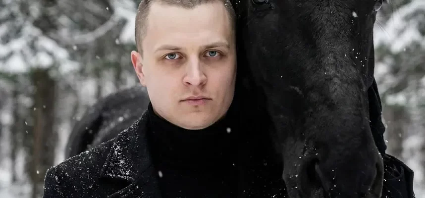 Мужчина в чёрном пальто с вороным конём в заснеженном лесу