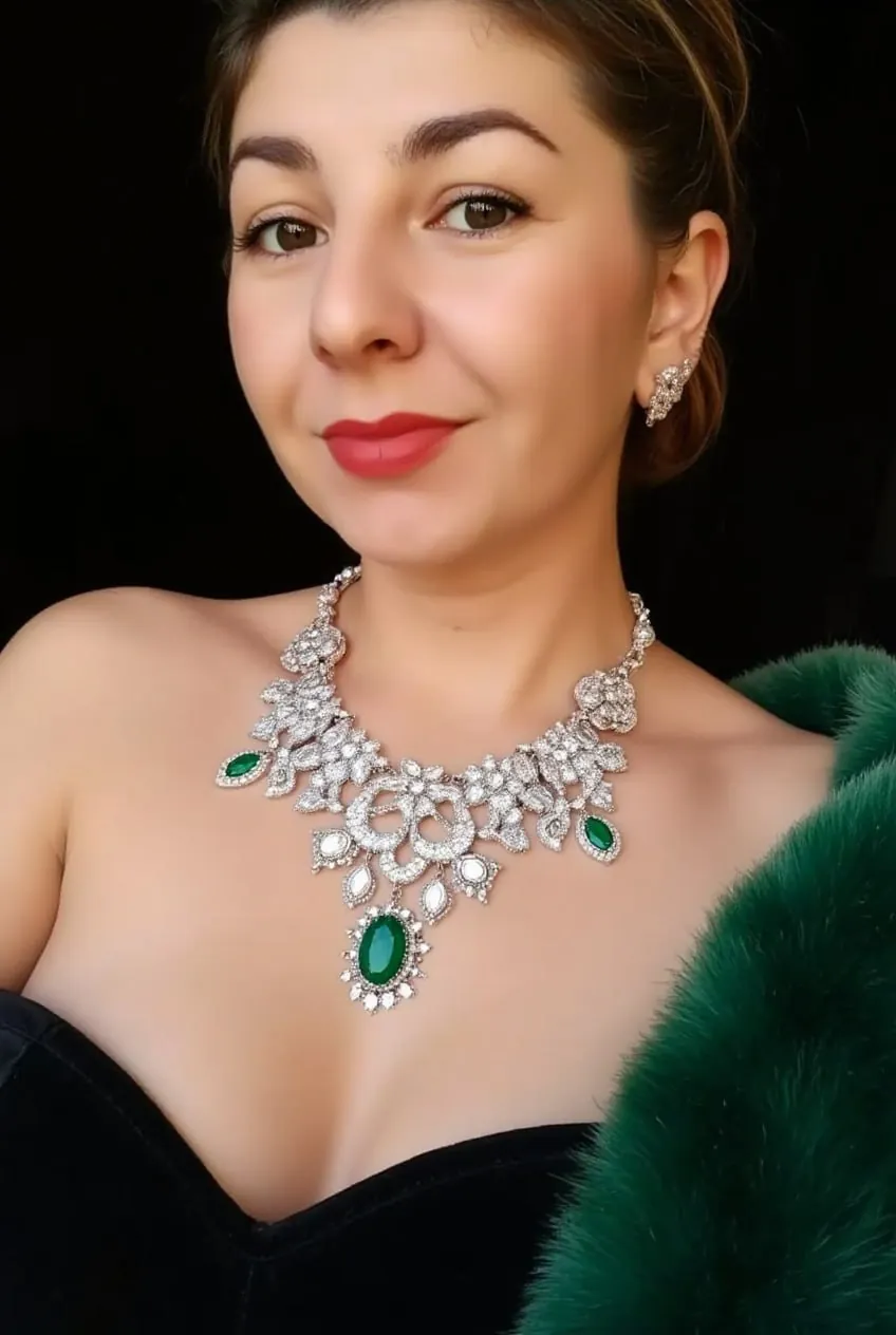 Женщина в чёрном платье и колье с изумрудом